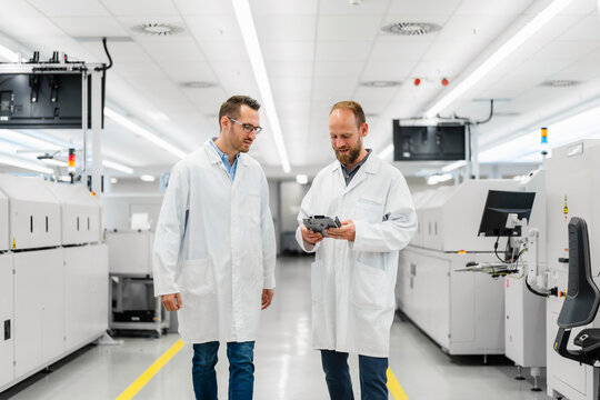 Technicians in white lab cots disussing over electronic component