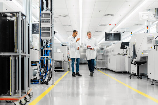 Discussing technicians walking through electronics factory holding motherboard