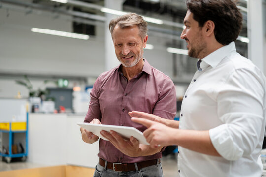 Smiling senior manager using tablet PC with colleague at factory