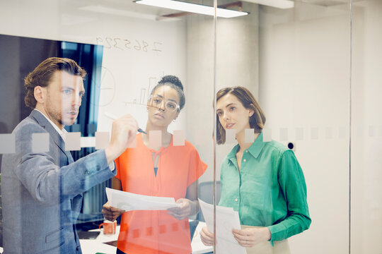 Businessman brainstorming colleagues standing behind glass wall - Powered by Adobe