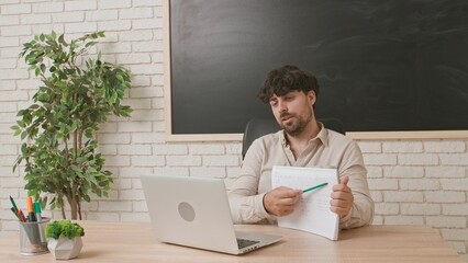 A male teacher talks to a student via video conference using a laptop and explains the lesson...