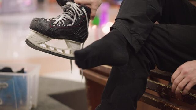 A close view of someone with a black ice skating shoe wearing black socks, as he dangle his leg, with blue skating shoe in a container by the side