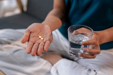 Obraz premium A woman is holding a glass of water and two pills in her hand