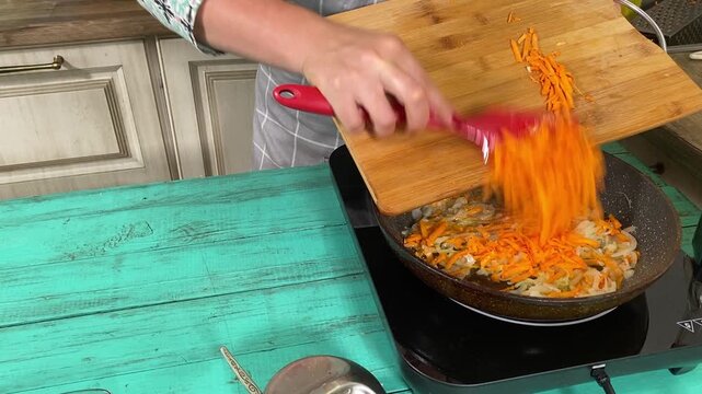 Culinary concept, preparation ingredients for homemade food. A young adult beautiful woman in an apron cooking a meal, makes mirepoix on a kitchen counter indoors. Home cooking and gastronomy passion