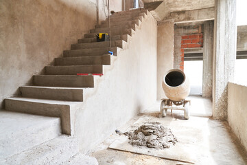 Concrete mixer and mortar by staircase inside incomplete house at construction site