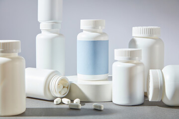Advertisement pic with pharmaceutical theme from over white background. Plenty medicine jars without label displayed on the gray table, a blue label one stands out on the podium