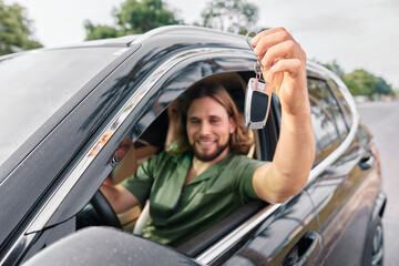 Naklejka premium Happy man showing car keys from a modern SUV while sitting in the driver s seat on a sunny day