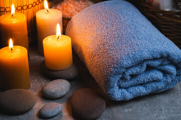Spa still life with candles, towel and stones on grey background.