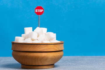 Sugar cubes in wooden bowl with red stop sign on blue background.