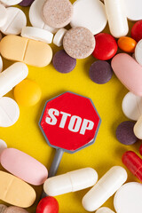 Red stop sign surrounded by many pills and capsules over yellow background.