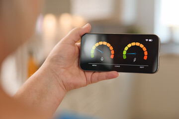 Person Holding Smartphone Displaying Energy Consumption Meter in Bright Indoor Environment During...