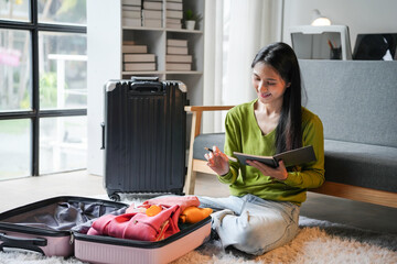 Young woman is sitting on the floor writing in a notebook with a suitcase open in front of her