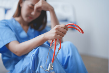 Young female doctor in blue scrubs is feeling overwhelmed and stressed while sitting on the floor...
