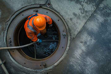A worker in safety gear conducts maintenance inside a circular underground tank with dark liquid, emphasizing safety and industrial practices.