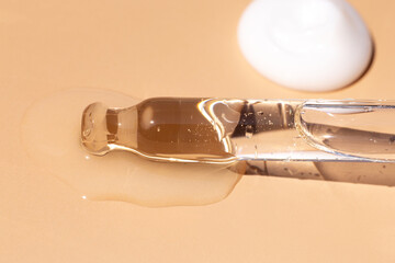 serum pipette close-up with falling drop on a beige background