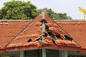 An abandoned building with some of the roof tiles falling off, leaving a hole in the roof.