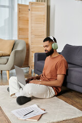 Man enjoying productivity while seated on the floor with his laptop and headphones.