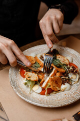 handsome man is eating  delicious salad with juicy chicken, fresh vegetables, and aromatic herbs with crispy croutons under a creamy sauce on a beautiful white plate in a cozy and nice restaurant