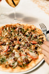 handsome man is eating delicious pizza with juicy sausages, fresh tomatoes, green aromatic herbs, and creamy cheese on a wooden board, which is on a beautiful white tablecloth
