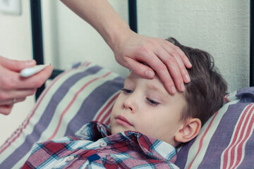 A mother measures the temperature of a sick child, carefully supporting him at the time