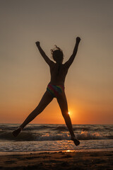 Kind springt am Strand zum Sonnenuntergang - Gegenlichtaufnahme im Wasser