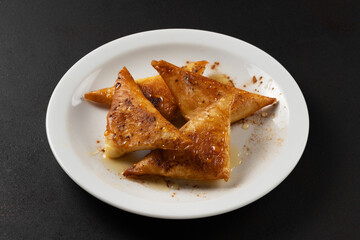 Mini cheese pies with myzithra, cretan honey and cinnamon on white plate.