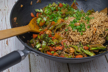 Mixed veggie and noodle stir fry in wok on white wooden background