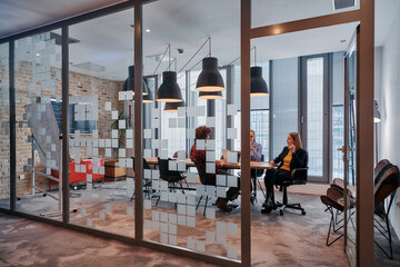 In the dynamic hustle and bustle of a business environment, a group of young business professionals walk down the corridor next to their office, while their colleagues collaborate inside, symbolizing