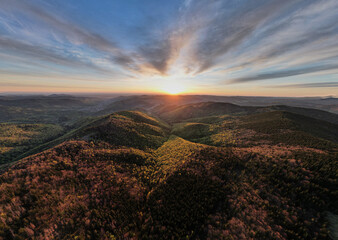 Aerial view of breathtaking sunrise over rolling mountains covered in mix of lush green and...