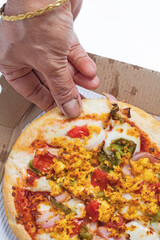 Pizza with paneer and cheese in a cardboard box with the hands of a woman on a white background. Top view