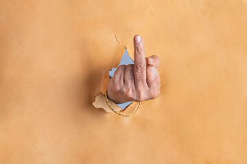 Indian woman hand showing middle finger gesture through the torn holes of brown paper background.