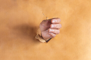 Hand coming out of a hole in a brown paper with copy space. Closeup