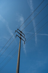 High voltage power line pole in a field. Low angle show, blue sky in the background, no people
