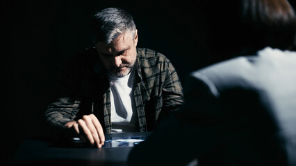 Detective showing photos of the crime scene to a male suspect in an interrogation room