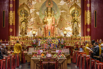 Interior view of a Buddhist Temple in Singapore, an altar with images of the buddha, monks and worshippers.