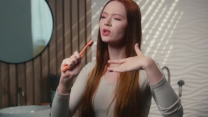 Happy Caucasian funny carefree woman singing song in toothbrush microphone sing dance at home bath morning beauty routine hygiene having fun brush teeth girl ginger female listen music in bathroom