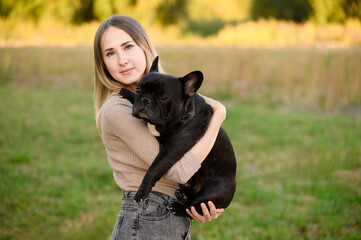 Woman hugging, holding her beloved pet French bulldog, smiling while holding him close, during...