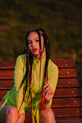 A woman with dreadlocks and a neon green dress sits on a wooden bench