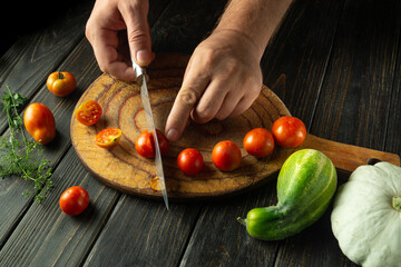 A cook prepares a vegetable lunch on the kitchen table. Slicing cherry tomatoes before cooking. Tomato diet menu