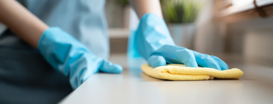 Housekeeper doing chores concept, Close-Up view of housemaid cleaning furniture surface with sanitizer spray and wiping with wet cloth in living room.