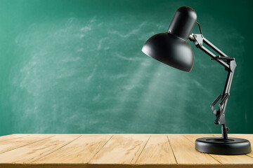 Black desk lamp on wooden table against green school chalkboard background. Back to school concept with copy space. Empty background.