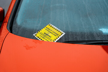 Bright Orange Car Displaying Penalty Charge Notice on Rainy Day