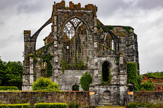 Front view of ruined former Aulne Abbey building, stone walls, wild green vegetation and trees, stormy sky covered with clouds in background, cloudy day in Thuin, Wallonia, Belgium