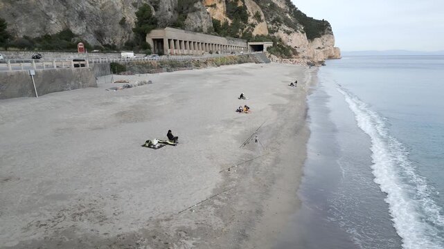 Dran flying over the sand of the beach with few people near the road