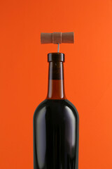 Wine bottle with corkscrew on orange background