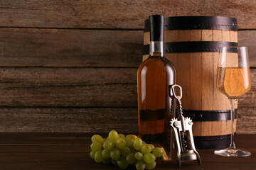 Obraz premium Glass of wine, bottle, wing corkscrew, barrel and grapes on wooden table, space for text