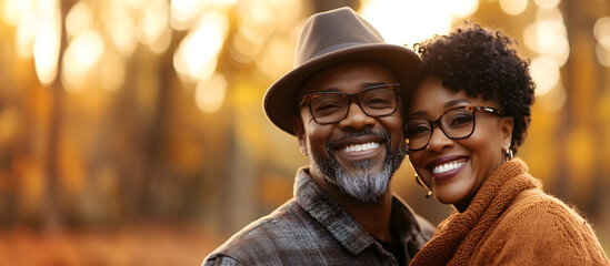 portrait of middle age african american couple standing outside; autumn/fall forest as a background; black retired husband & wife standing outside and hugging; copy space