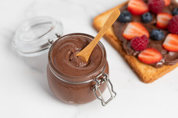 Chocolate butter, chocolate-nut paste in a glass jar on a light table, American breakfast