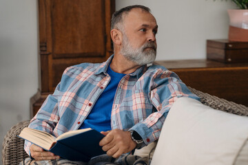 Fototapeta premium Man Sitting Comfortably in Cozy Living Room Reading Book During the Afternoon