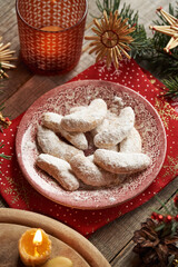 Homemade Christmas cookies called Kipferl or vanilla crescents coated in sugar on a red plate with decorated spruce tree